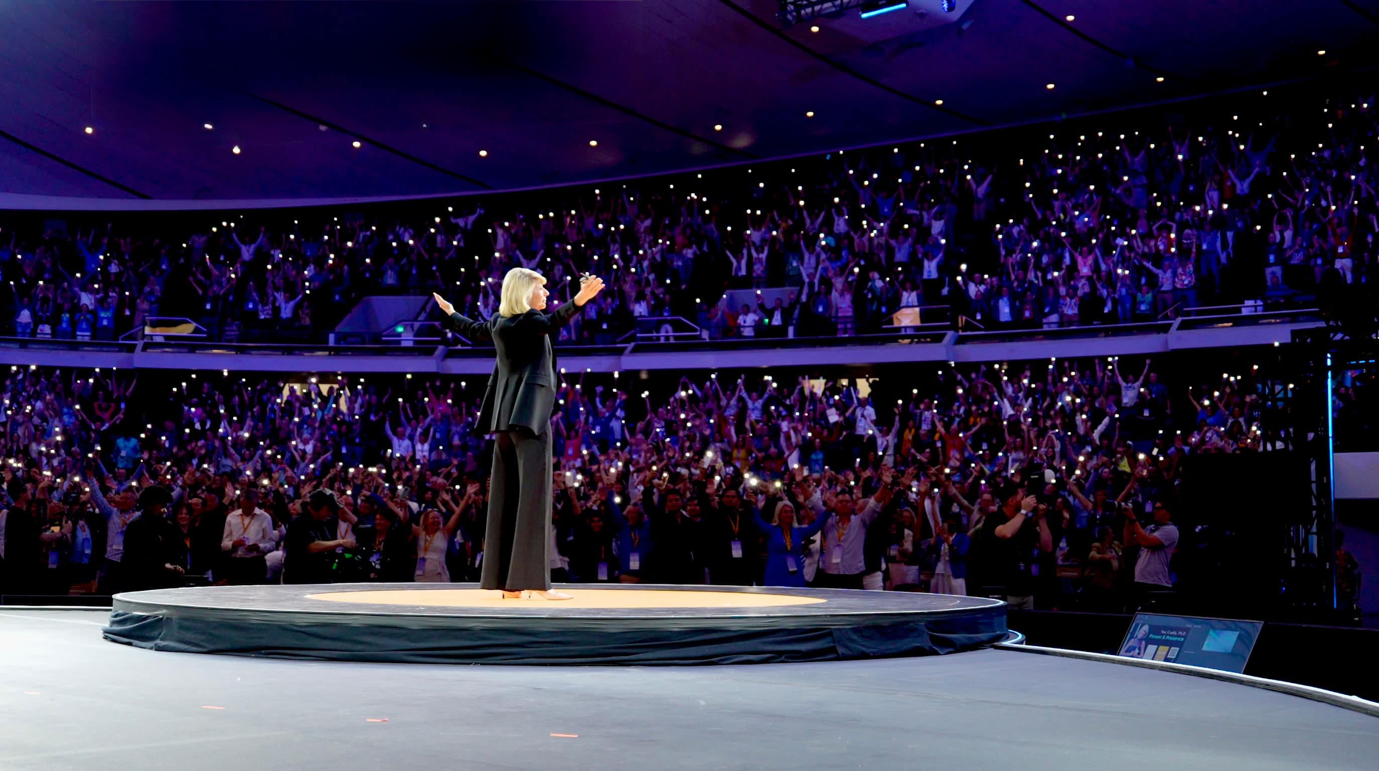 Amy Cuddy on stage before a packed arena, arms open to the audience